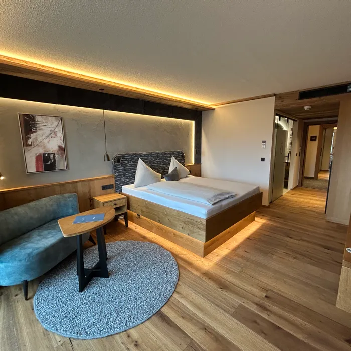 Camera d'hotel moderna con pavimento in legno, letto matrimoniale, divano e illuminazione soffusa